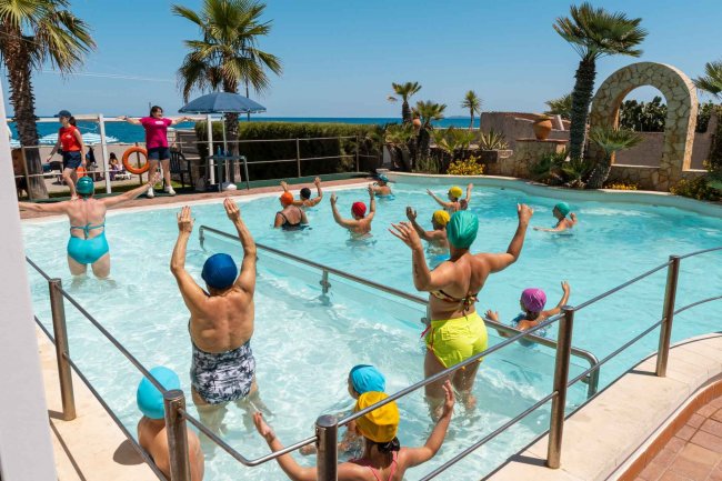 Persone che fanno acquagym in una piscina all'aperto con vista mare.