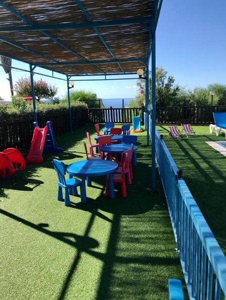 Un'area giochi per bambini con tavolini e sedie colorate sotto una tettoia azzurra.