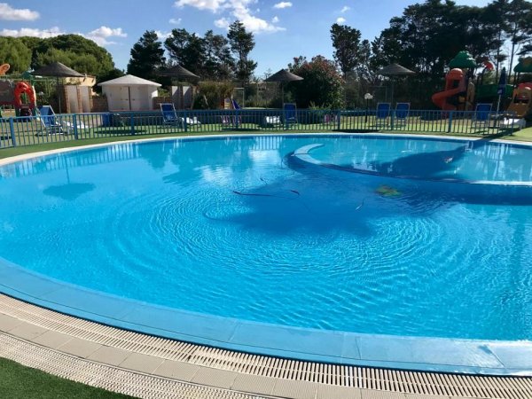 Piscina circolare all'aperto con recinzione blu e giochi per bambini sullo sfondo.