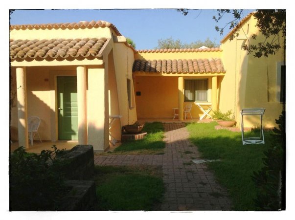 Esterno di edificio giallo con tetto in mattoni e cortile verde.