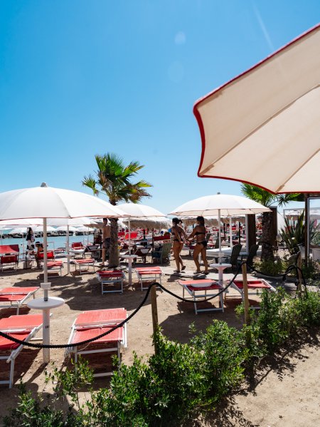 Spiaggia con lettini rossi e ombrelloni bianchi.