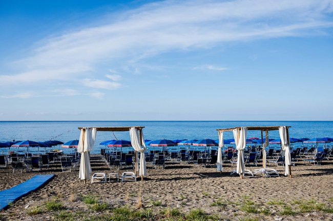 Spiaggia con ombrelloni e gazebo bianchi.
