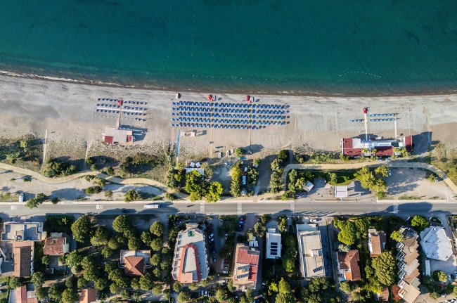 Spiaggia vista dall'alto con ombrelloni e strada adiacente.