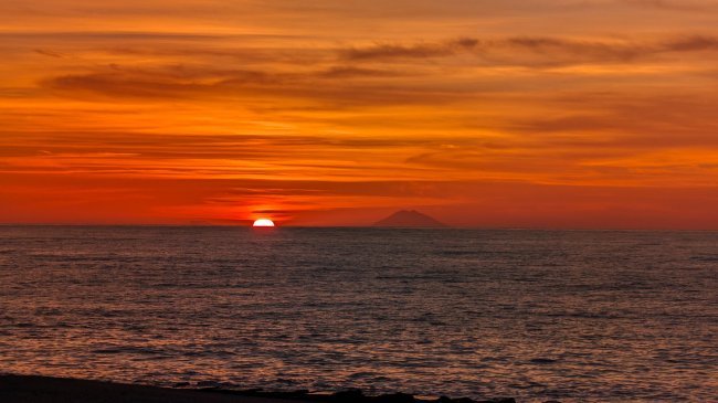 Tramonto sul mare con il sole parzialmente visibile all'orizzonte.