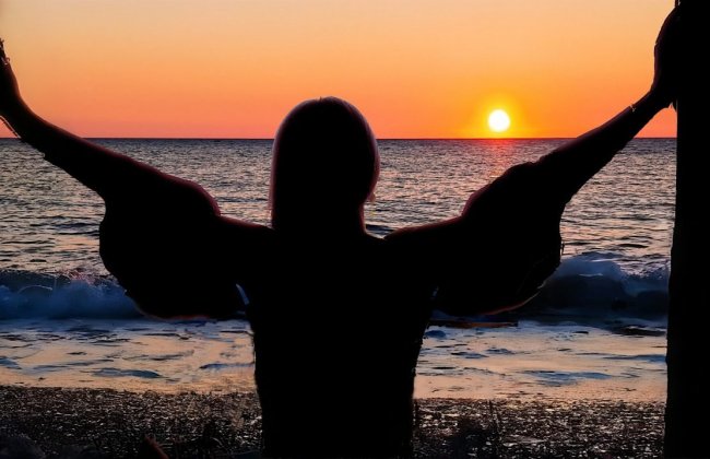 Silhouette di una persona che guarda un tramonto sul mare.