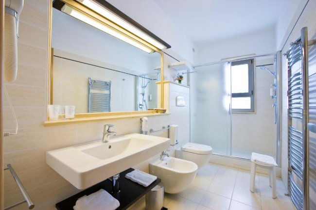 Un bagno moderno con lavabo, bidet e doccia. Piastrelle chiare e ampia specchiera.