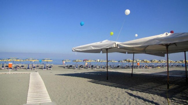 Una spiaggia con lettini e ombrelloni gialli sotto un cielo blu.