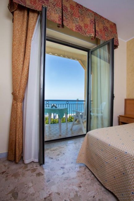Porta finestra aperta su un balcone con vista mare.