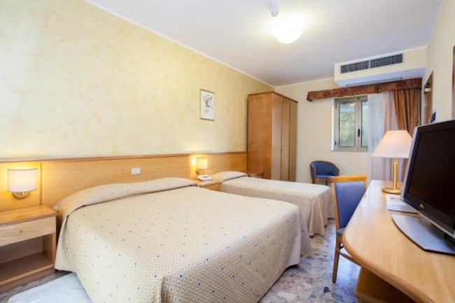 Camera d'albergo con due letti matrimoniali, scrivania, TV e finestra.