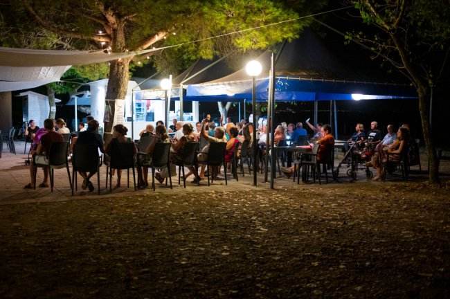 Persone sedute a tavoli all'aperto, illuminate da luci notturne.