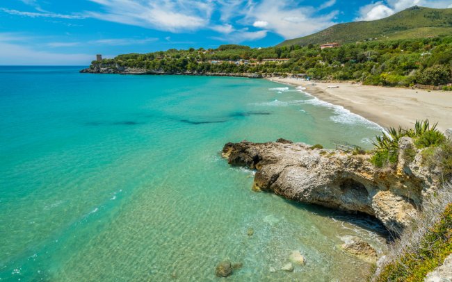 Spiaggia con mare turchese, sabbia chiara e scogli.