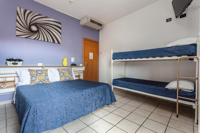 Stanza da letto con letto matrimoniale e letto a castello, pareti bicolore, aria condizionata e TV.