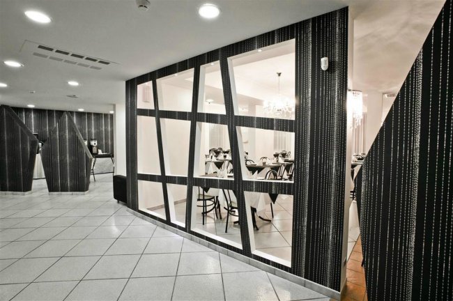 Corridoio moderno in bianco e nero con vetrate inclinate che rivelano una sala da pranzo con sedie.