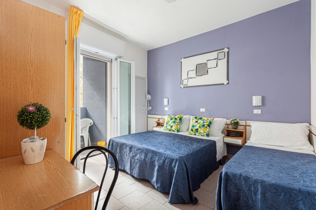 Camera d'albergo con due letti matrimoniali, cuscini colorati e un balcone.