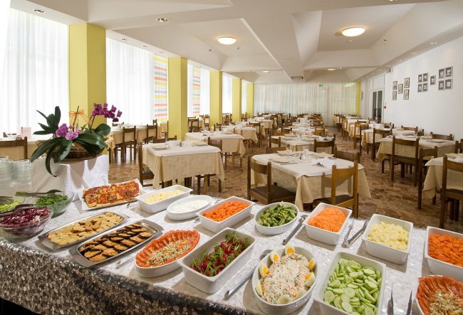 Sala da pranzo con tavoli coperti e buffet di verdure.