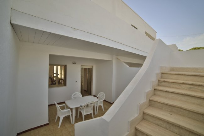 Patio con tavolo e sedie bianche accanto a una scala.