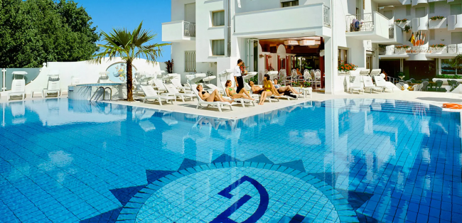 Piscina all'aperto con lettini e palme.