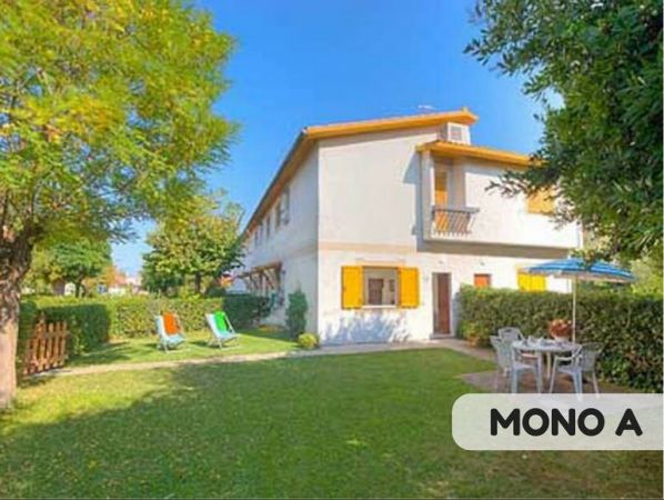 Casa a due piani con giardino, sedie a sdraio e tavolo all'aperto.
