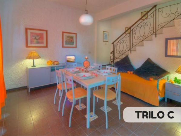 Sala da pranzo con tavolo, sedie bianche, scala e divano arancione.