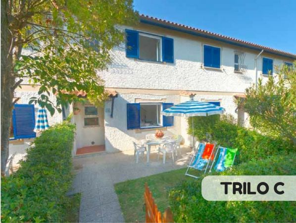 Casa bianca a due piani, giardino con ombrellone e sedie a sdraio.