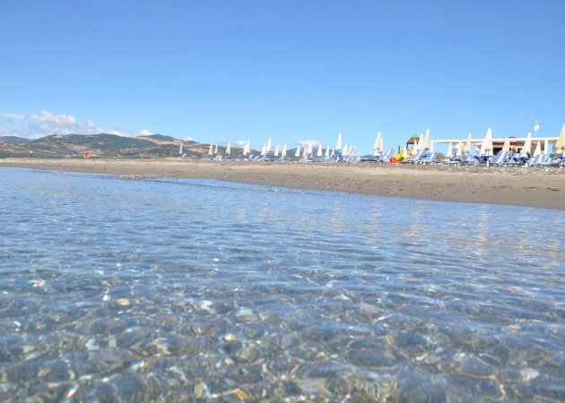 Spiaggia con acqua cristallina e ombrelloni in lontananza.