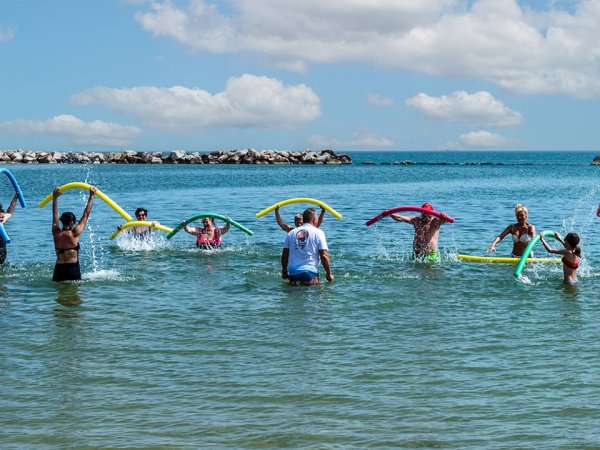 Persone in mare con tubi galleggianti colorati.