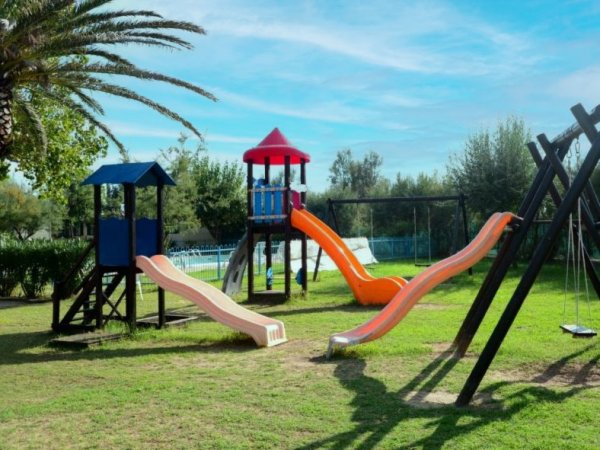 Parco giochi con scivoli e altalene su prato.
