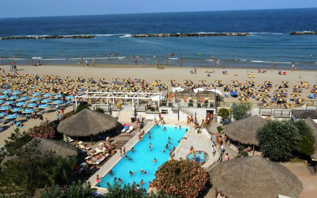 Piscina e spiaggia con ombrelloni vicino al mare.