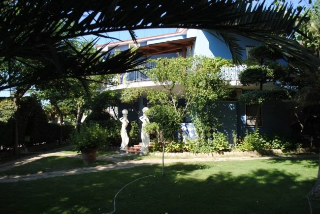 Giardino con statue bianche e una casa blu.