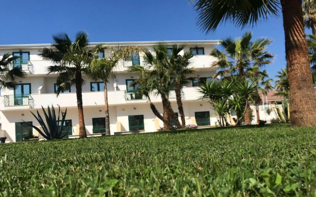 Edificio bianco tra palme su un prato.