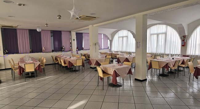 Sala da pranzo con tavoli apparecchiati e finestre ampie.