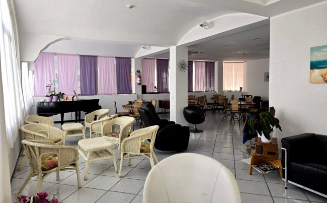 Sala con sedie in vimini e pianoforte. Finestre con tende viola.
