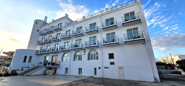 Edificio bianco a più piani con balconi, cielo azzurro e nuvole.
