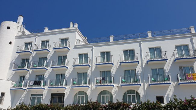 Edificio bianco a tre piani con balconi e cielo azzurro.
