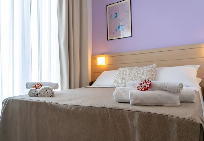 Stanza con letto matrimoniale, asciugamani piegati e parete lilla.