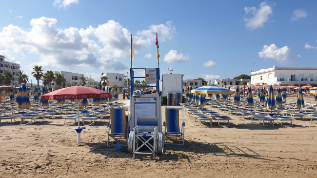 Spiaggia con sdraio blu e gialle, ombrelloni e cielo nuvoloso.