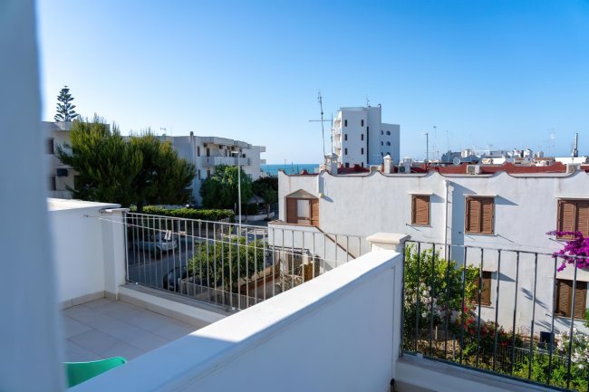 Terrazza con vista su edifici, alberi e mare in lontananza.