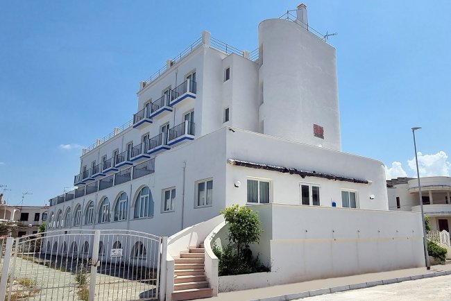 Un edificio bianco a più piani con balconi blu e scale esterne, sotto un cielo sereno.
