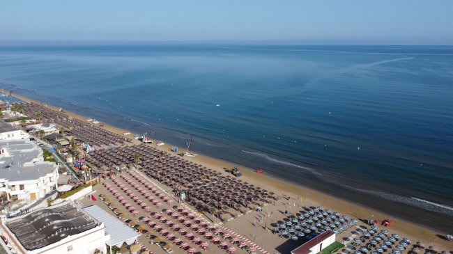 Spiaggia con file di ombrelloni e mare calmo.