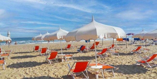 Una spiaggia con ombrelloni bianchi e sedie a sdraio rosse.