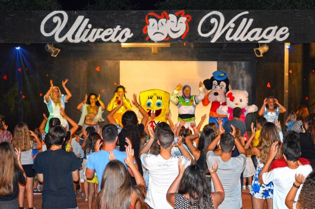 Persone ballano sul palco con personaggi in costume.